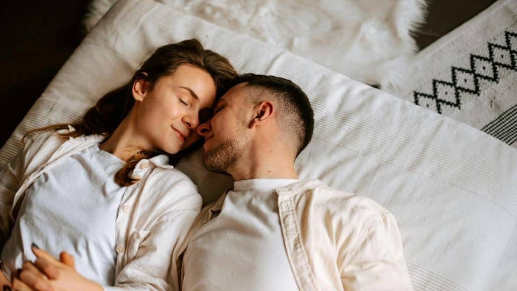 A couple lying close together on a bed smiling at each other.