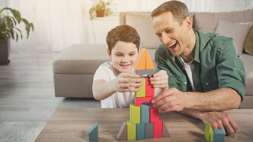 Smiling father and son building a colorful rocket-shaped structure with blocks.