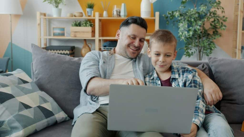 Smiling father and son looking at a laptop together on a couch.