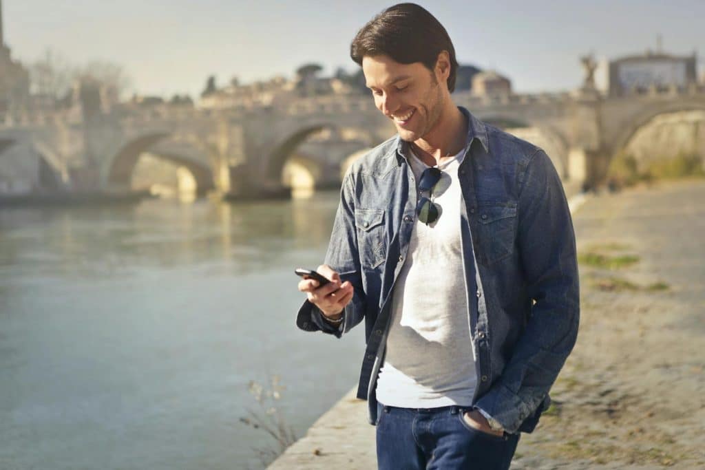 The man is texting someone while he’s walking near the river.
