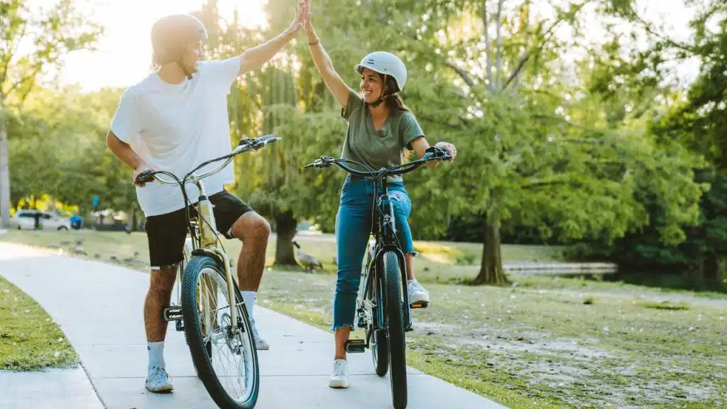 A couple riding bicycles in a park giving each other a high five.