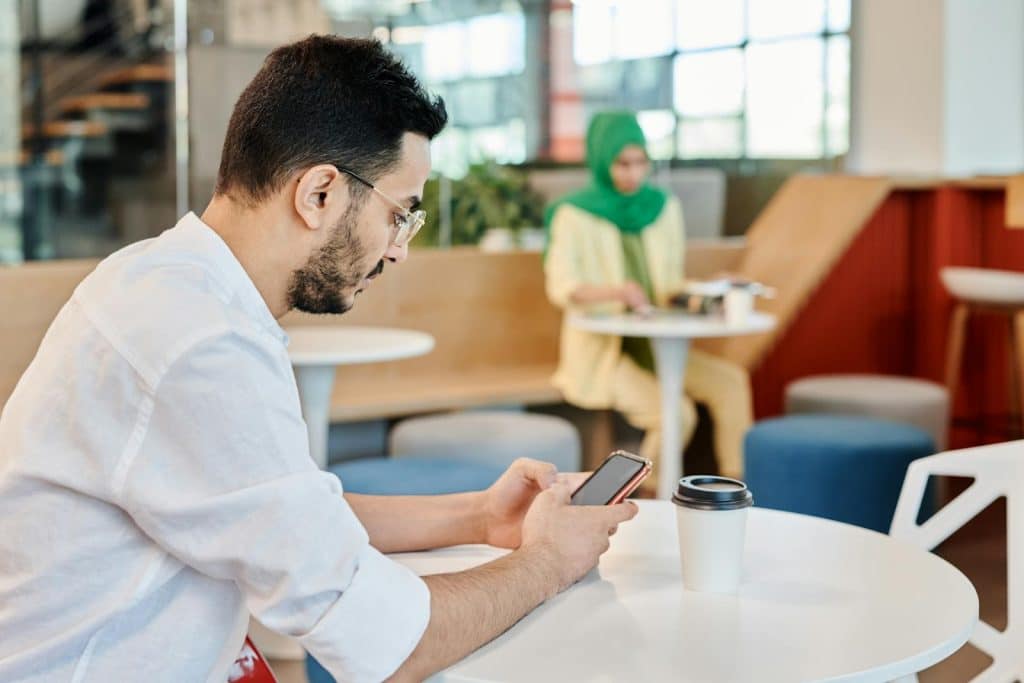 The man is holding his phone while waiting at a cafè.