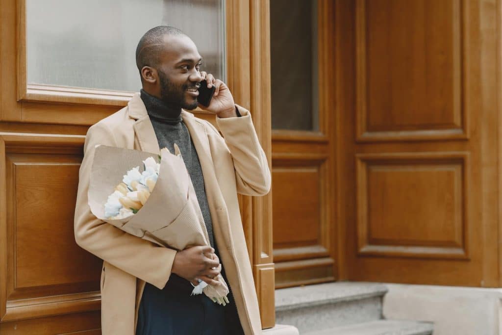 The man is holding a bouquet while calling someone.