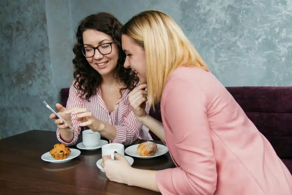 The women are looking at the phone while spending time in a café.