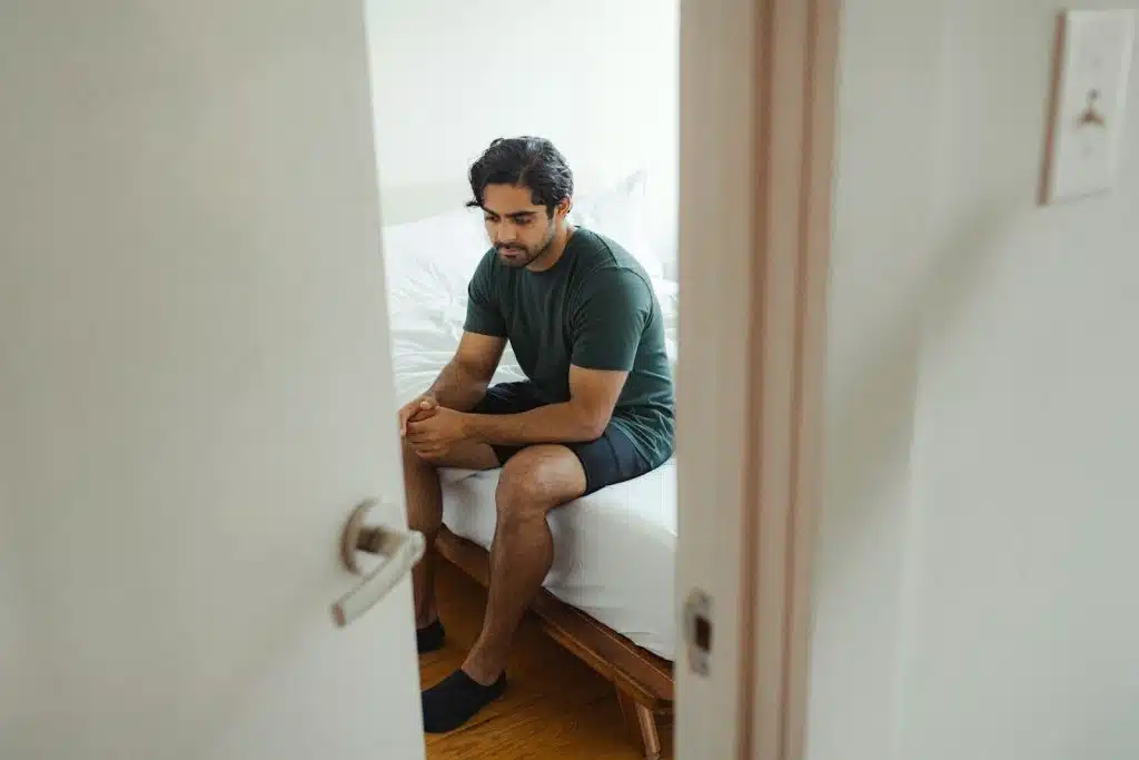 The sad man is sitting on the edge of the bed.