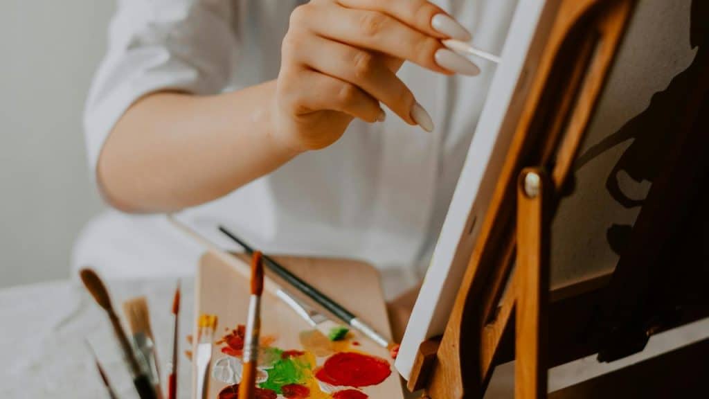 A person painting on a canvas with brushes and a palette nearby.