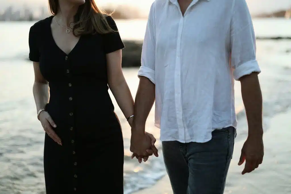 The couple is walking on the beach while holding each other’s hands.