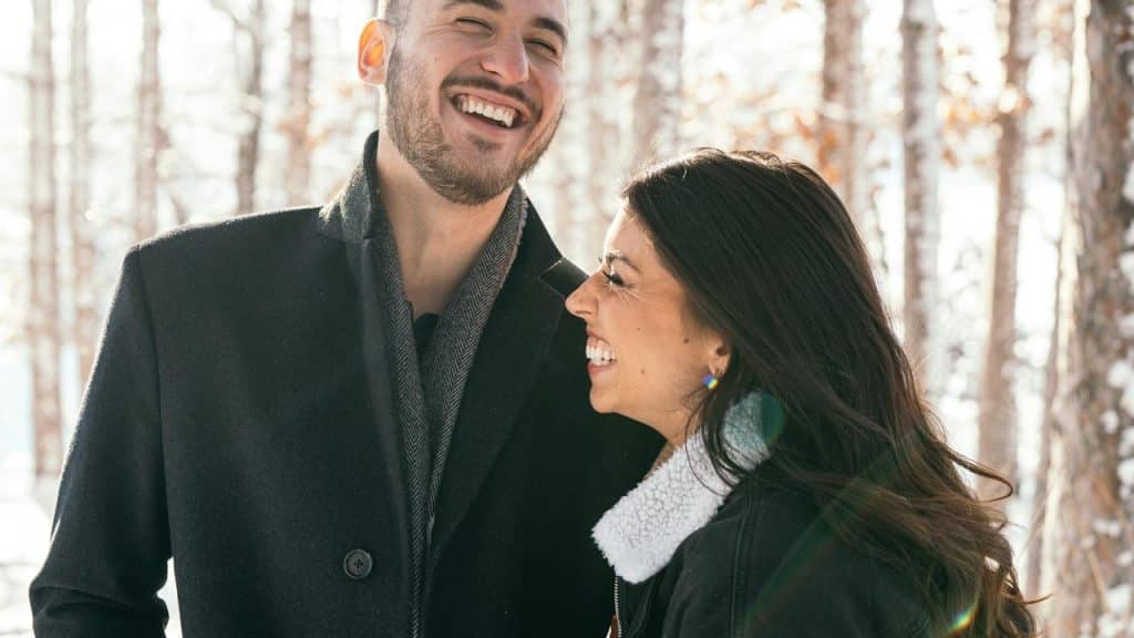 A couple laughing together outdoors in a snowy forest.
