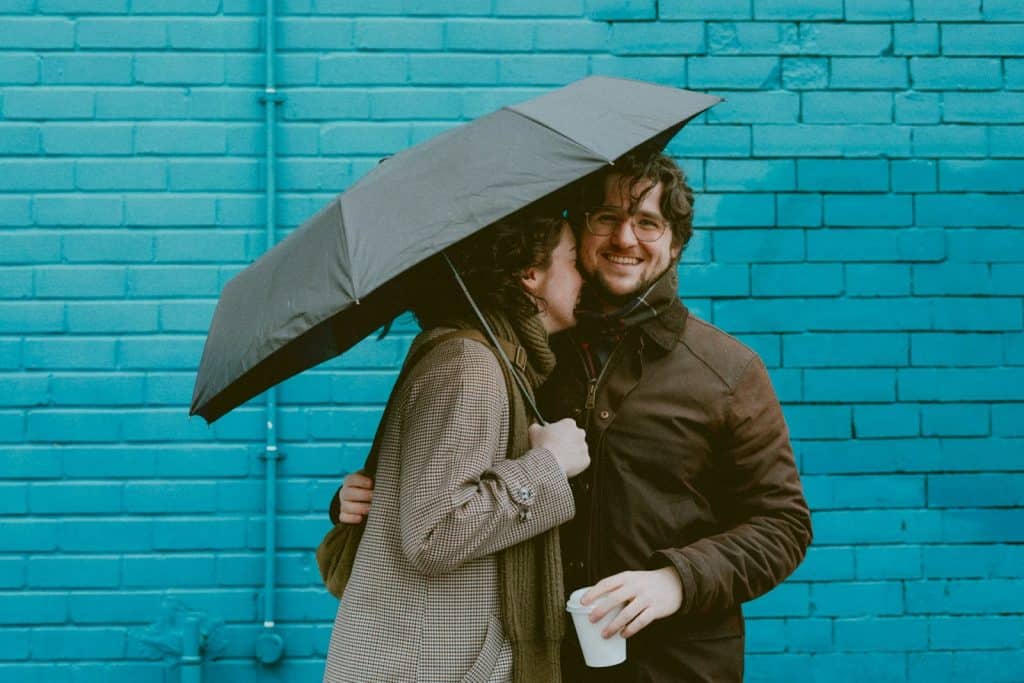 The woman holding the umbrella is hugging the man.
