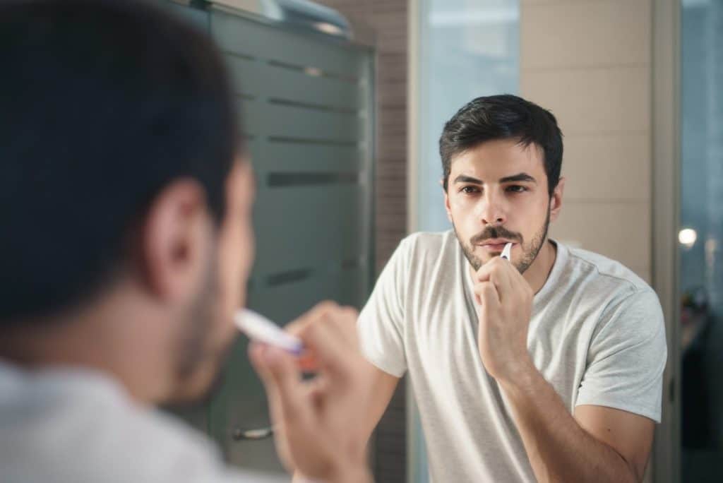 The man is brushing his teeth in front of the mirror.