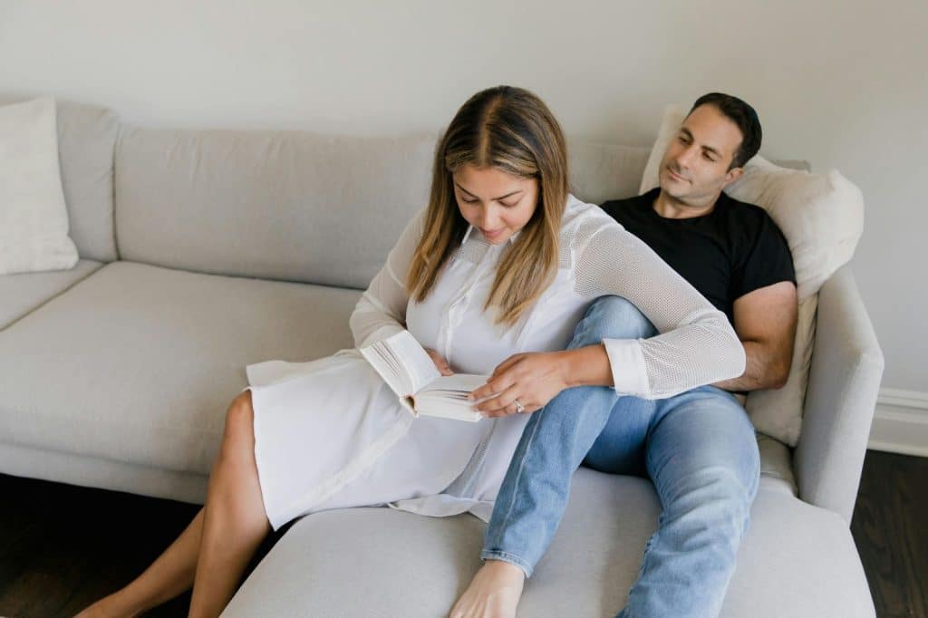 A man looking at the woman while reading a book