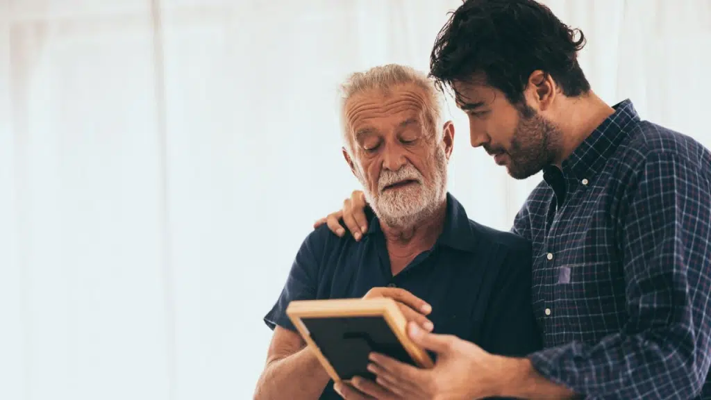 A young man with his arm around an older man looks at a framed photo with him.