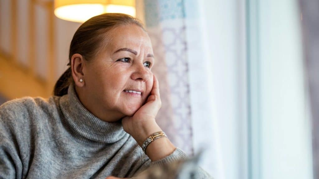 Close-up of a middle-aged woman wearing a gray turtleneck, looking out a window.