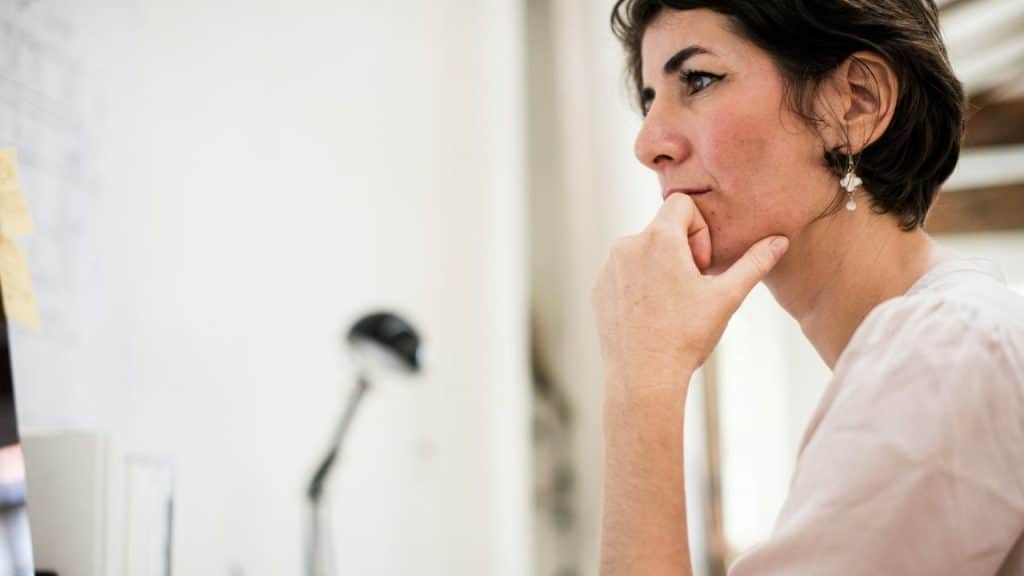 Close-up of a dark-haired woman in profile, chin resting on her hand, looking intently.