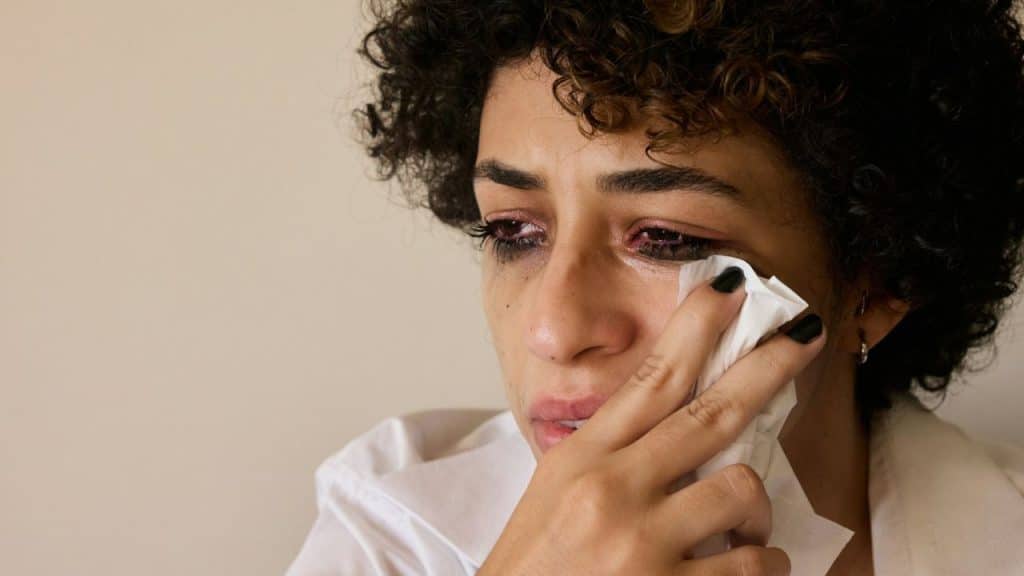 Close-up of a person with curly hair crying and wiping their eyes with a tissue.