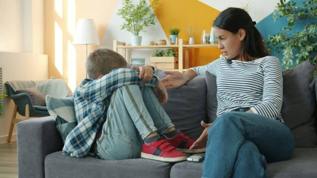 A woman attempts to comfort a young boy curled up and crying on a couch.