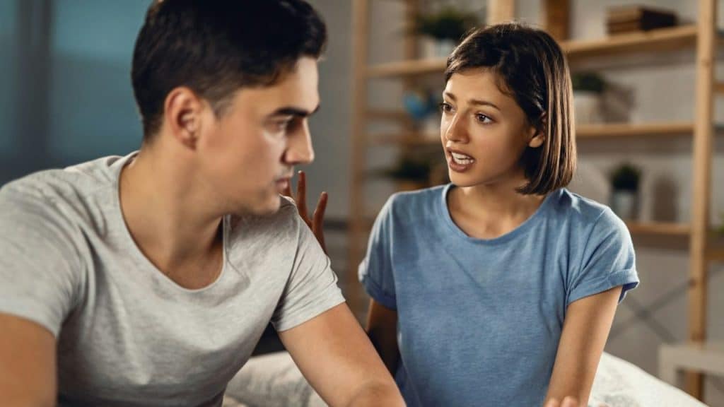 A young woman in a blue shirt is speaking intensely to a man in a gray shirt.