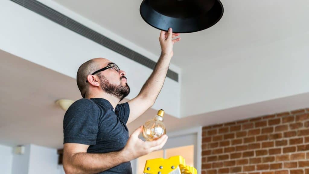 Man on a ladder changing a lightbulb in a black overhead light fixture.