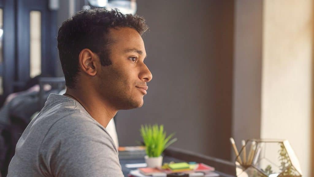 A close-up side profile of a man with dark, curly hair looking into the distance.