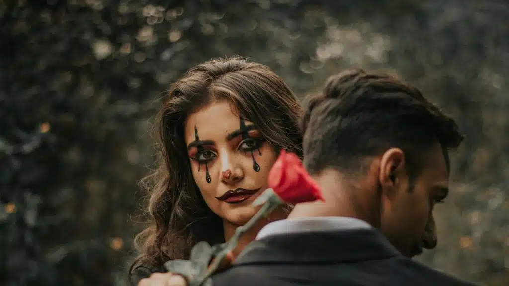 A woman with clown makeup holding a red rose.