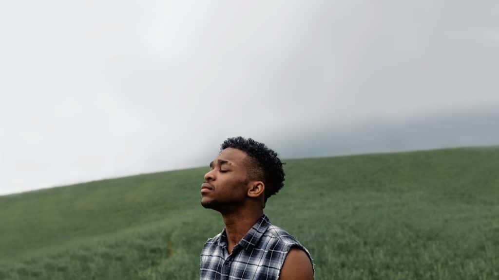 A sad man standing in a grass field.