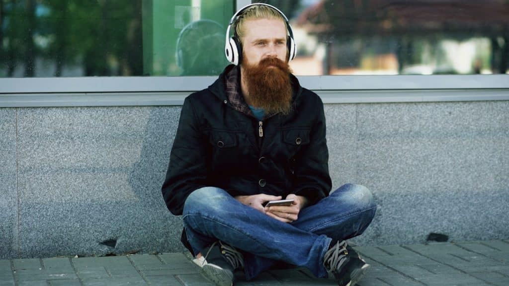 A man with a beard and headphones sitting outdoors.