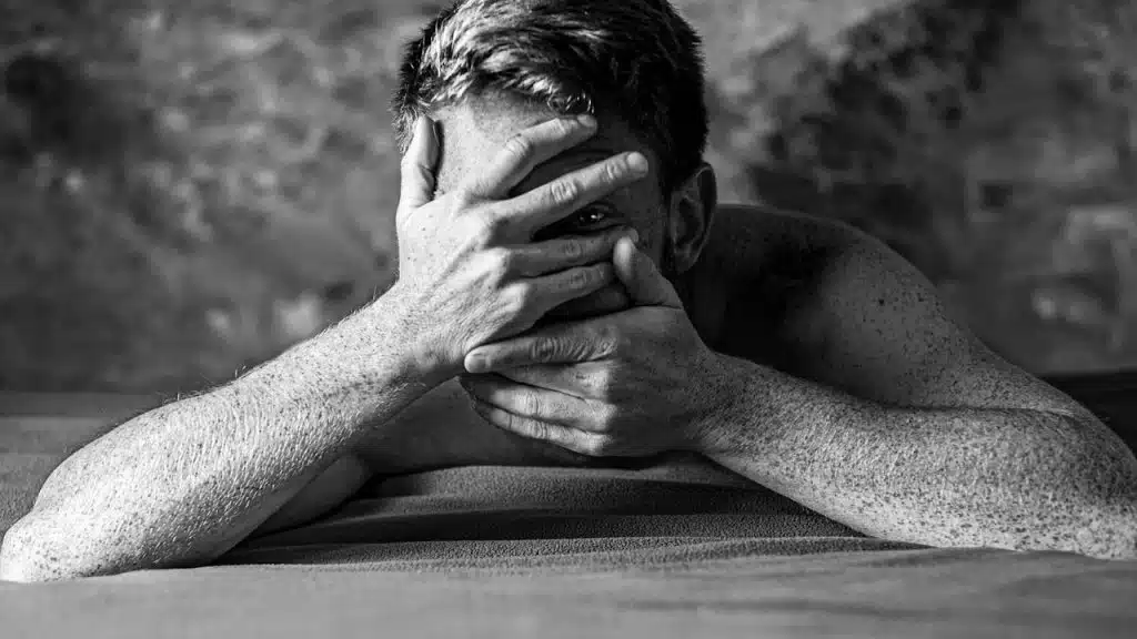 A grayscale image of a man covering his face with both hands