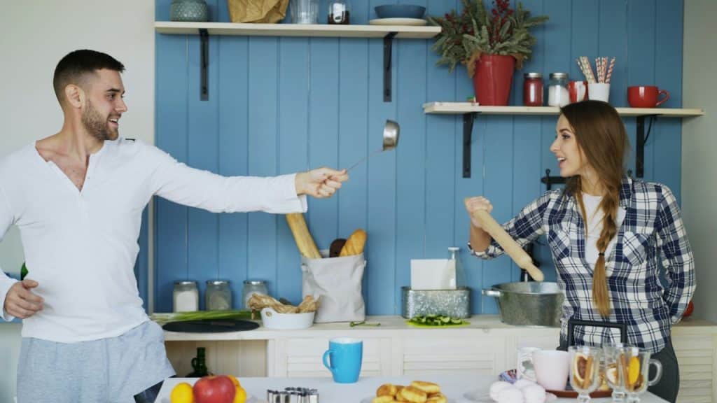 A couple having a cute fight with kitchen utensils.