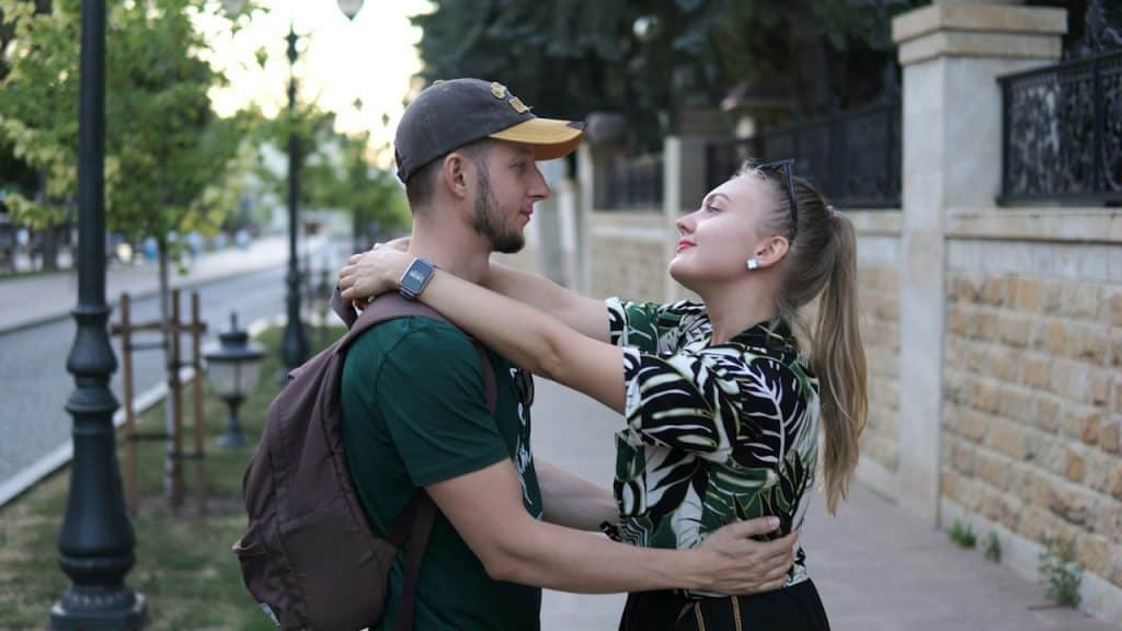 A couple standing with each other on a sidewalk.