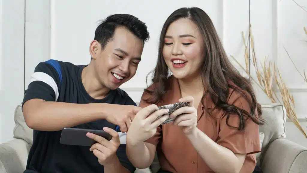 A man and a woman sitting and checking social media indoors.