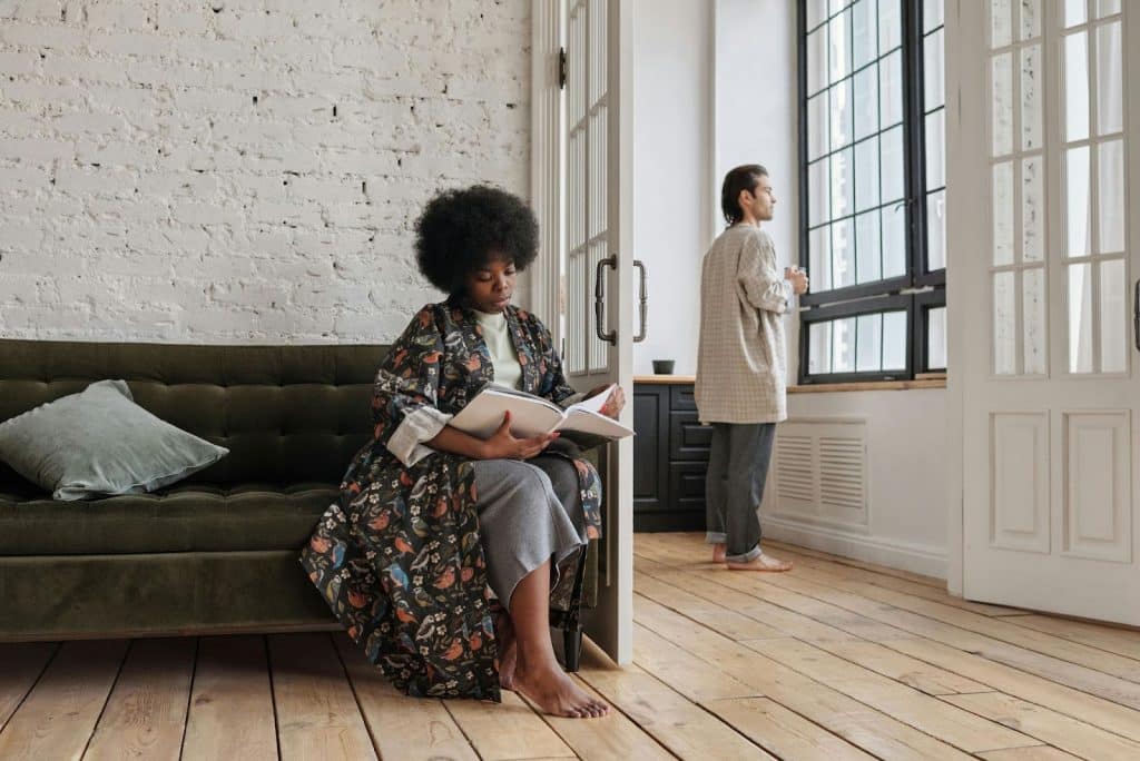 A man looking outside the window and a woman reading a book