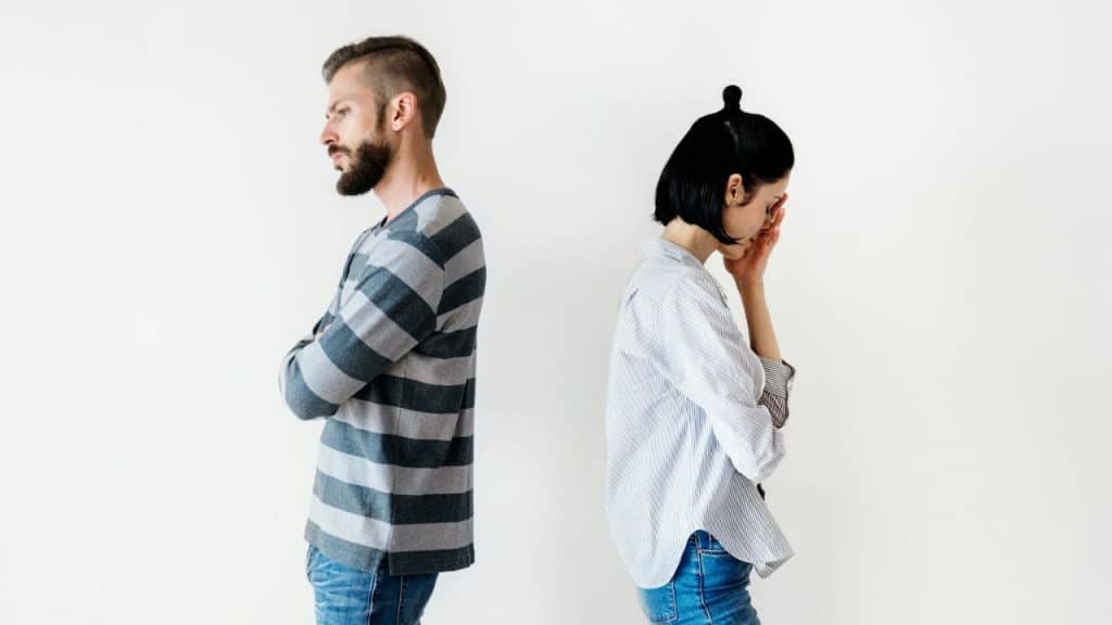 A man and woman stand back-to-back against a white wall after an argument.
