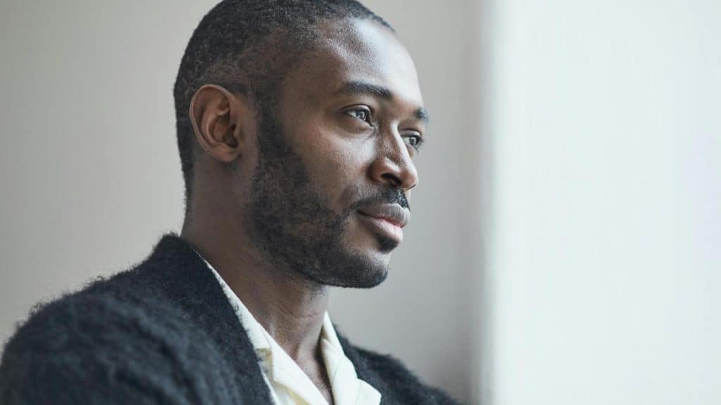 A man looking out of a window with a thoughtful expression.