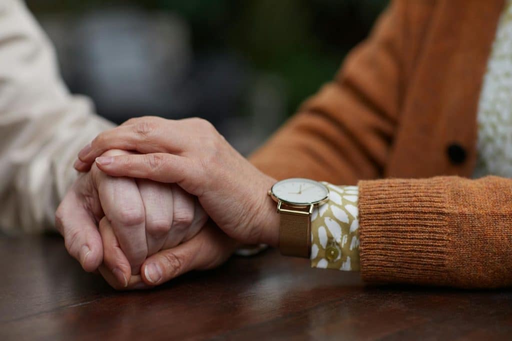 The elderly couple is holding each other’s hands.