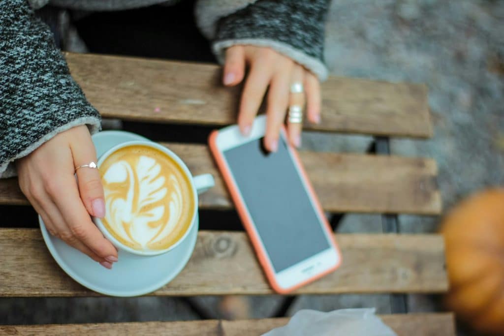 The woman is touching her cup of coffee and her phone.