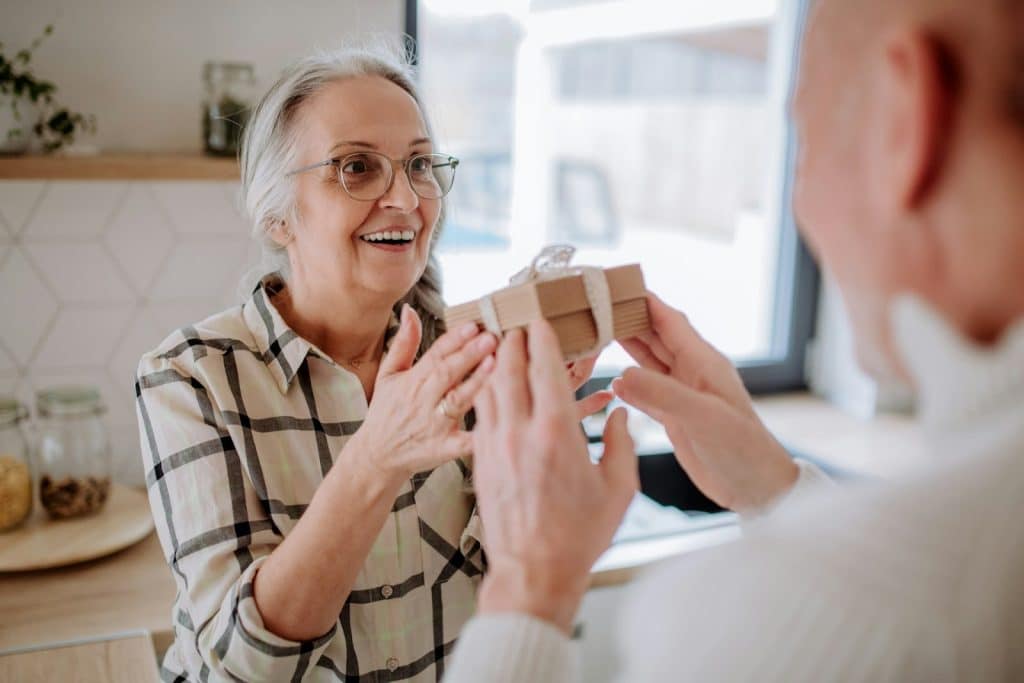 The senior woman is smiling as she receives the present from her husband.