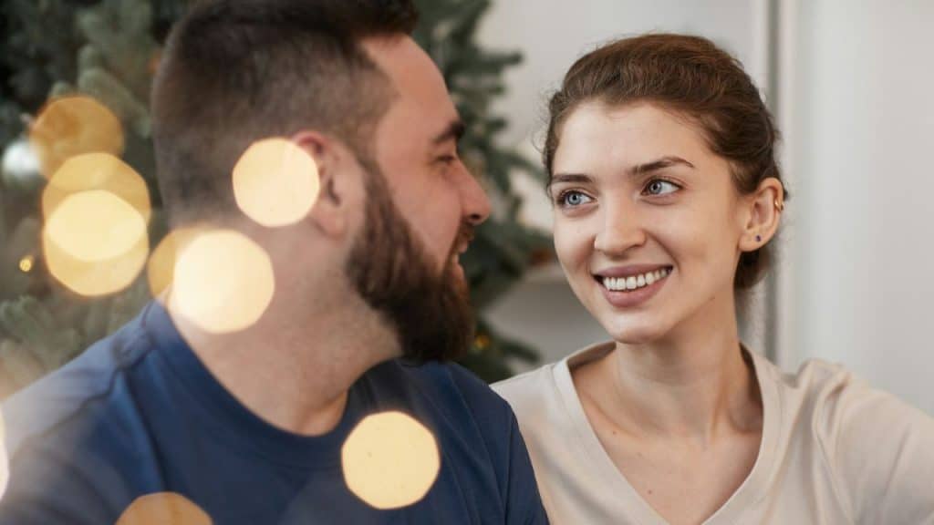 A happy man and woman are smiling at each other, with blurred lights in the foreground.