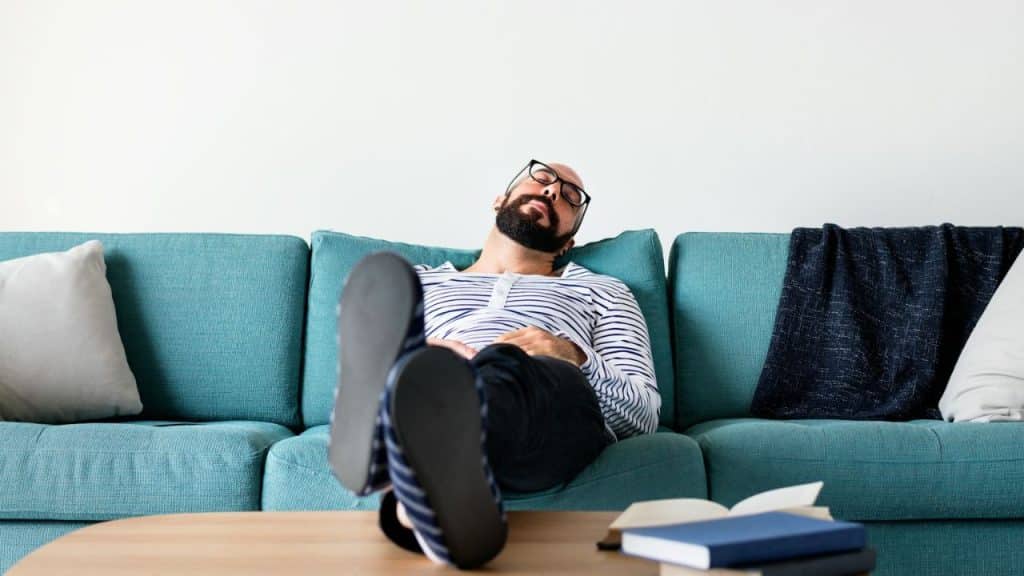 A man with a beard and glasses is napping on a teal couch.