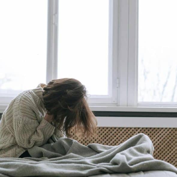 A person sitting on a bed with their head down, appearing distressed.