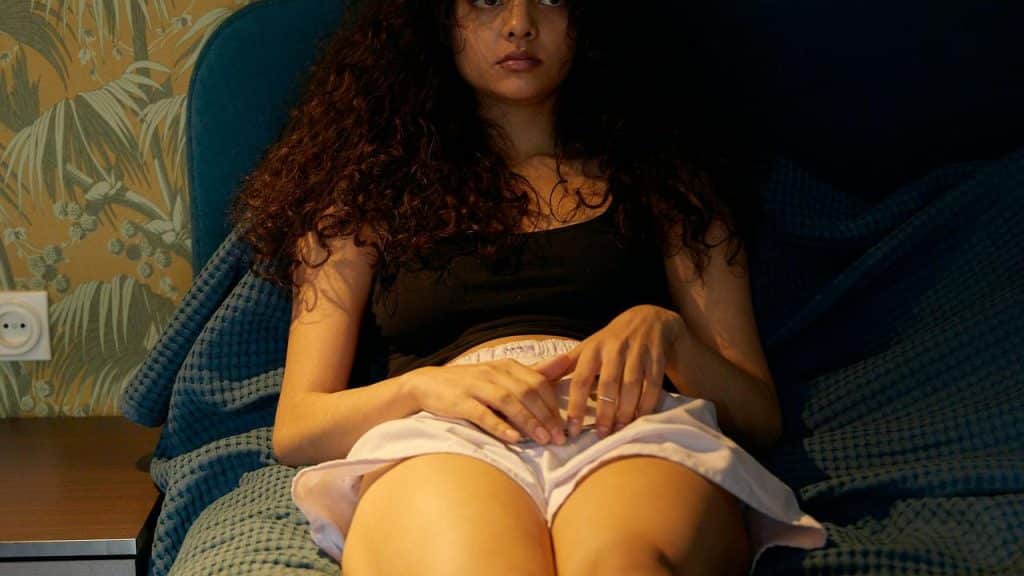 A person sitting on a bed looking thoughtful or concerned.