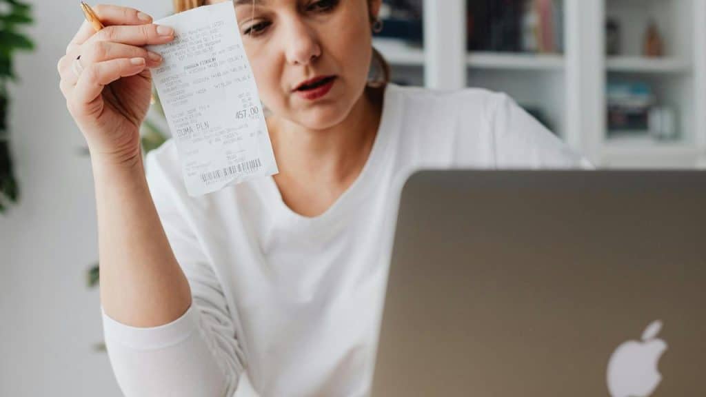 A person holding a receipt while looking at a laptop.