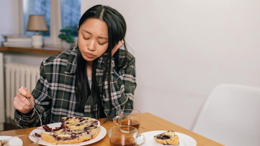 A person sitting at a table looking down while eating dessert.