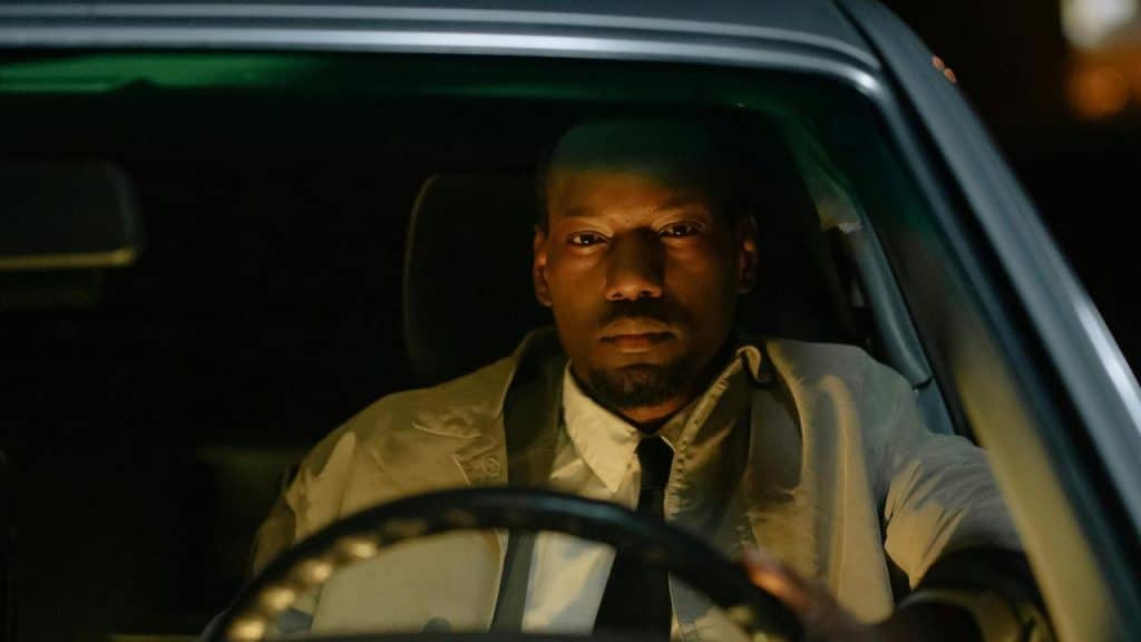 A person sitting in a car at night, looking forward seriously.