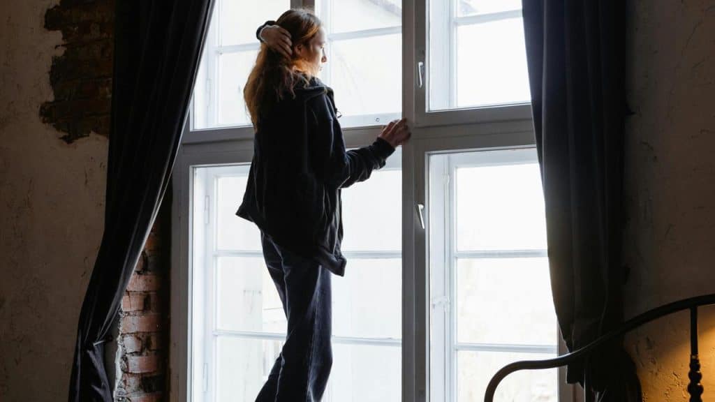 A person standing by a large window, looking outside thoughtfully.