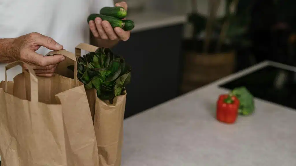 A person unpacking fresh vegetables from paper grocery bags.