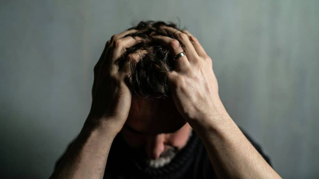 Close-up of a man with his hands clutching his hair, ring visible on his finger.