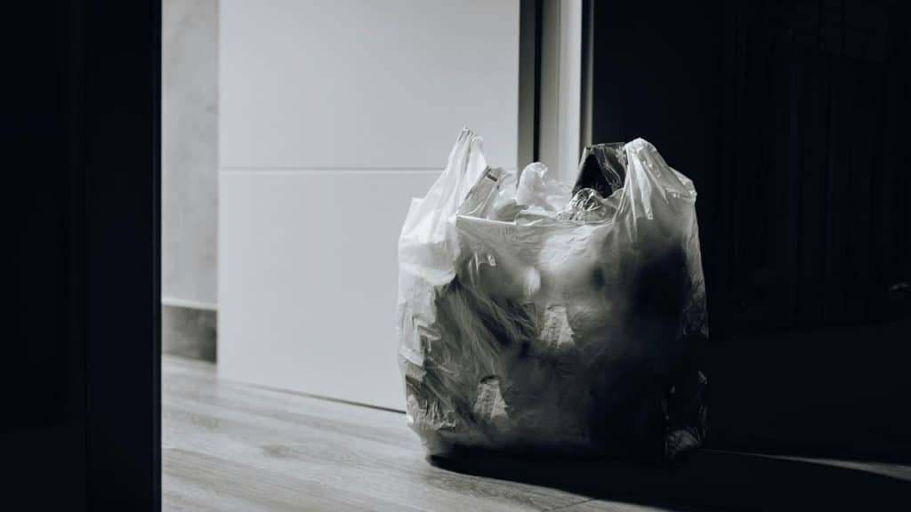 A plastic trash bag full of garbage placed on the floor near a doorway.