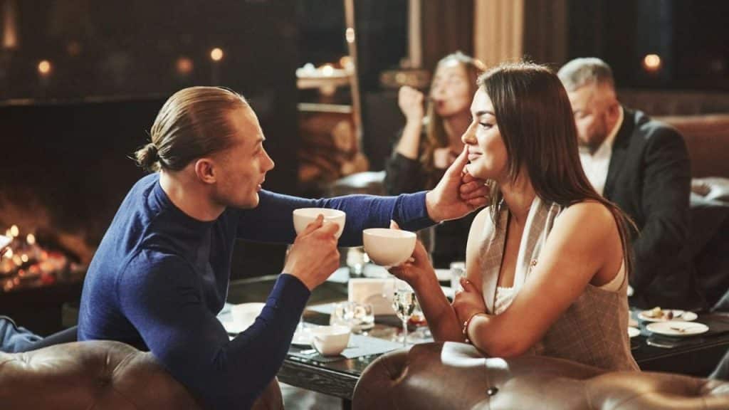 Man and woman on a date holding cups, the man touching the woman's cheek and smiling.