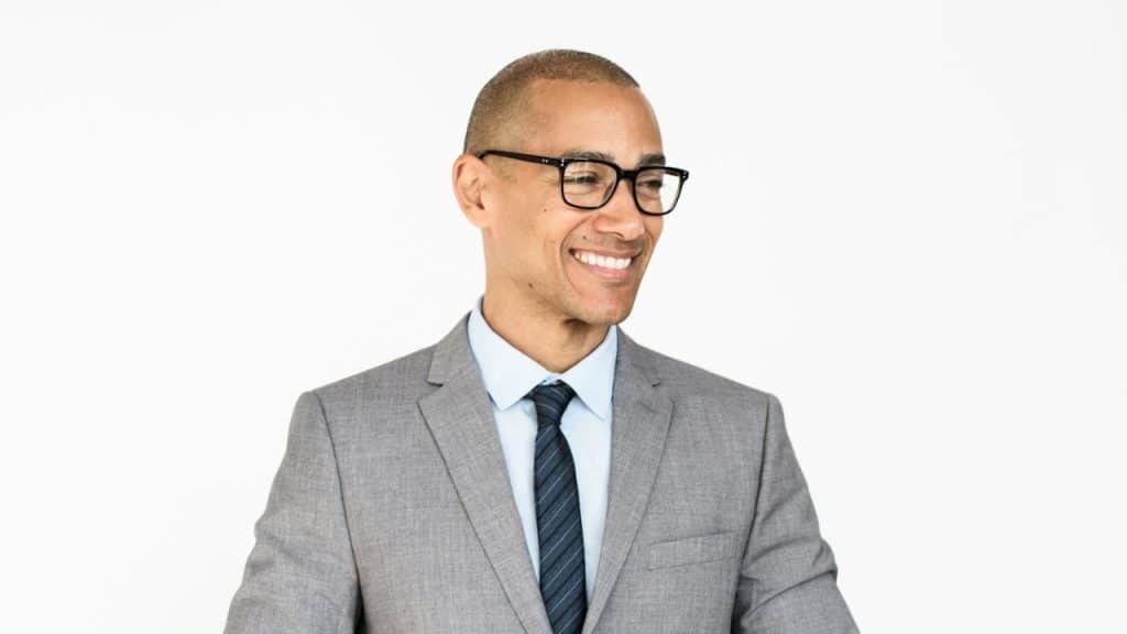 Smiling, bald man wearing a gray suit, blue shirt, and glasses against a white background.