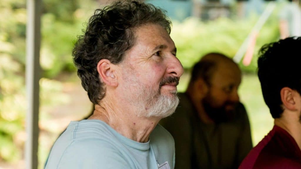 Older man with a gray beard and curly hair looking off to the side outdoors.